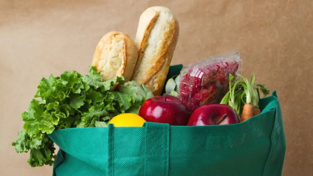 Close up of groceries like bread and produce sticking out of the top of a green bag
