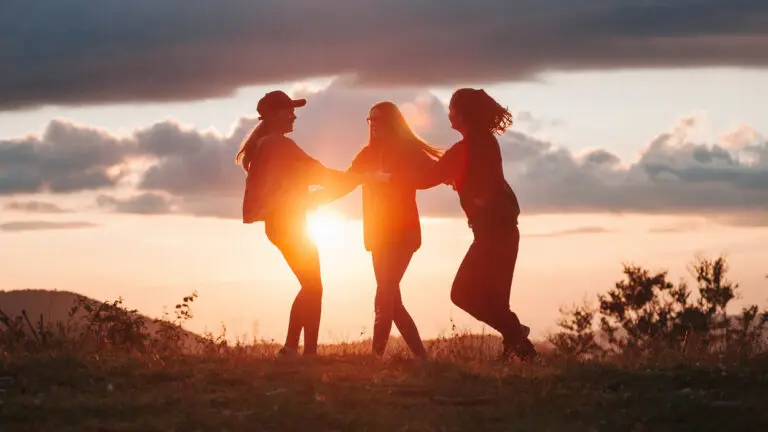 Three girls, in silhouette with the sun behind them, jump together.