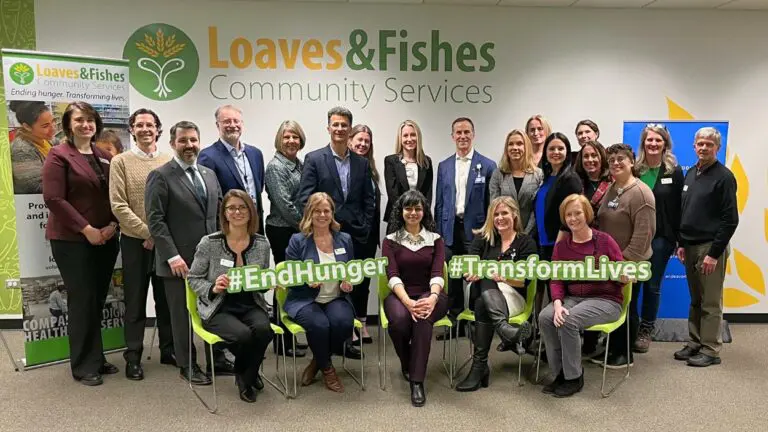 Officials from Loaves and Fishes and Endeavor Health are pictured smiling, holding signs that read "End Hunger," and "Transform Lives."