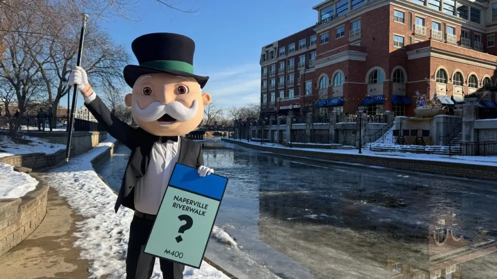 Mr Monopoly character from MONOPOLY board game standing on Riverwalk by DuPage River in Naperville
