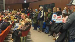 Group of peoplpe standing against back wall at city council meeting with some holding signs