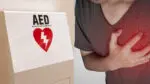 picture of man clutching chest while next to an AED device