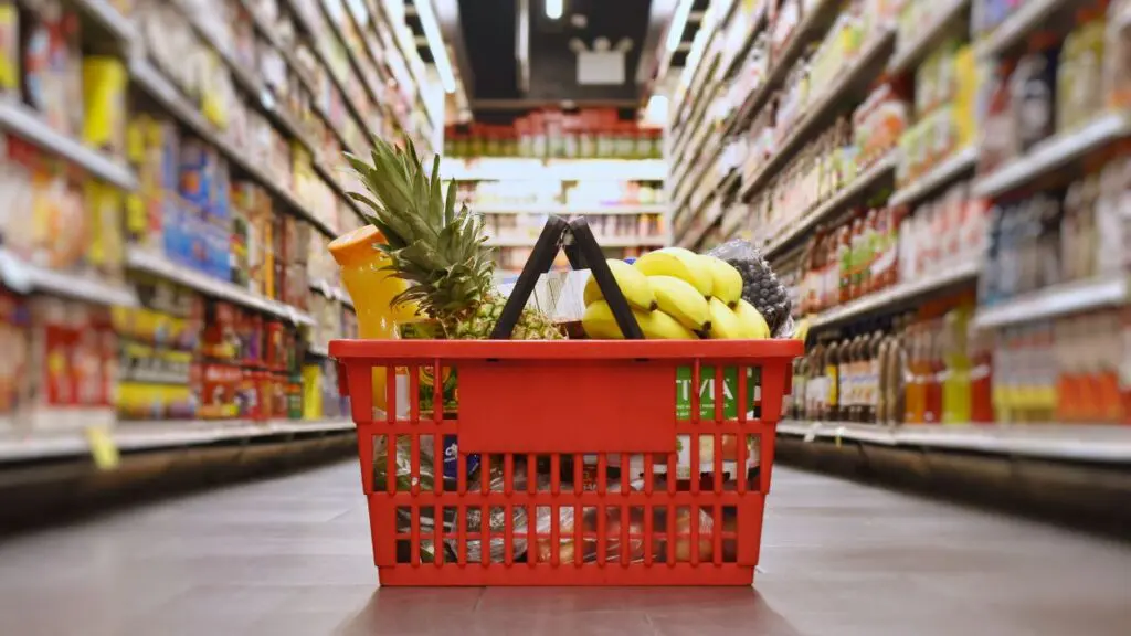 Grocery basket with groceries inside sitting in the middle of a grocery store aisle