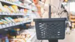 Person holding empty shopping basket standing in front of refrigerated case in grocery store