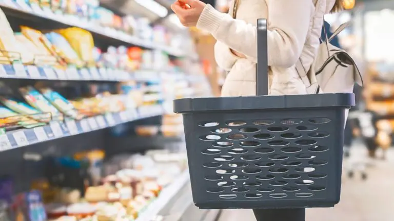 Person holding empty shopping basket standing in front of refrigerated case in grocery store