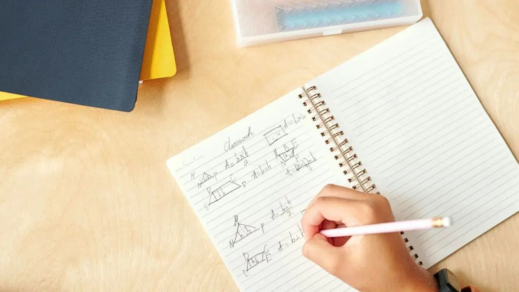 Geometry formulas written in open notebook with hand holding pencil in view