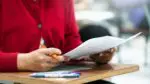 Close up of student in red sweater holding paper at school desk
