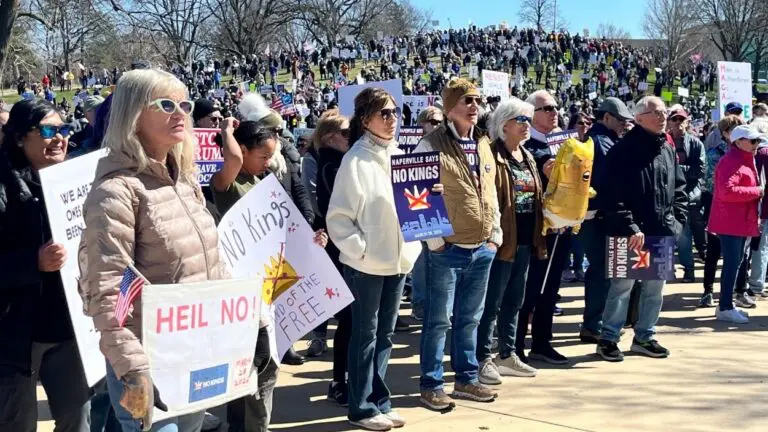 Dozens of people residents stand while holding "No Kings" signs at the Naperville No Kings Rally.