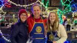 A trio of Naper Lights volunteers standing in front of a holiday display in downtown Naperville.