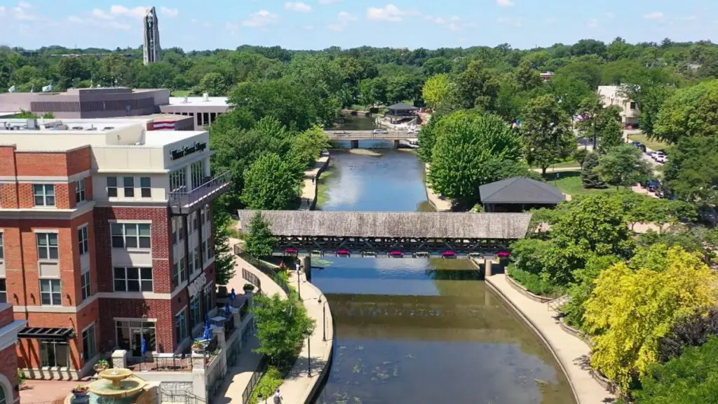 Drone shot of Naperville Rivewalk with covered bridge, DuPage River, and Moser Tower in view