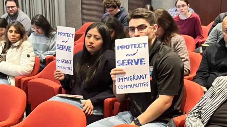 two people at Naperville City Council meeting holding up Protect and Serve immigrant communities signs