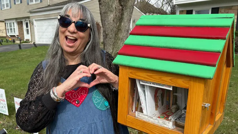 Karyn Ross of the Love and Kindness Project Foundation makes a heart shape with her hands as she stands next to her Kindness House, part of the Worldwide Sidewalk Joy initiative