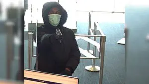 A man in seen pointing a gun inside a Bank of American branch in Naperville. He is wearing a surgical mask and a black sweatshirt.