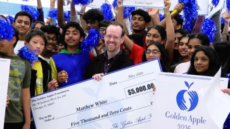 Naperville teacher and Golden Apple Award winner Matthew White smiles for a picture while surrounded by students and holding a check.
