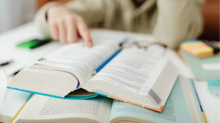 Close up of person reading with finger on book with two books in image