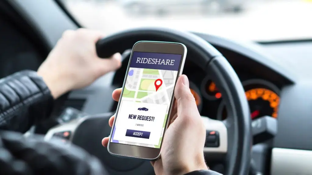 Close up of driver holding a phone with Rideshare app on it with steering wheel visible