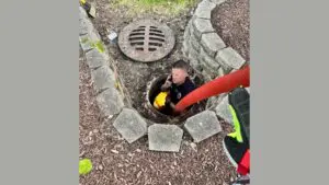 Naperville firefighter with hose in sewer hole for duckling rescue