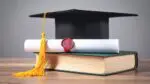 Graduation hat sitting atop a book with a diploma in the pile as well