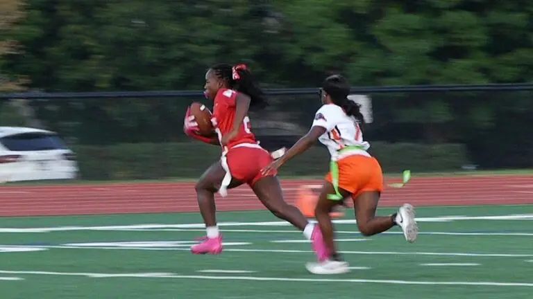 One girl chases another girl in a game of flag football.