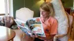 Naperville resident Ginny Wolf Chivas is pictured sitting on a chair reading Naperville Preservation Inc.'s new book, Don Tosi’s Naperville, A 2025 Architectural Survey.