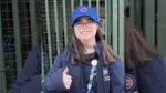 Lily Goodfellow outside Wrigleyfield wearing cubs gear giving a thumbs up