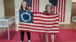 Abby Douglass and a volunteer hold up the handcrafted American flag.