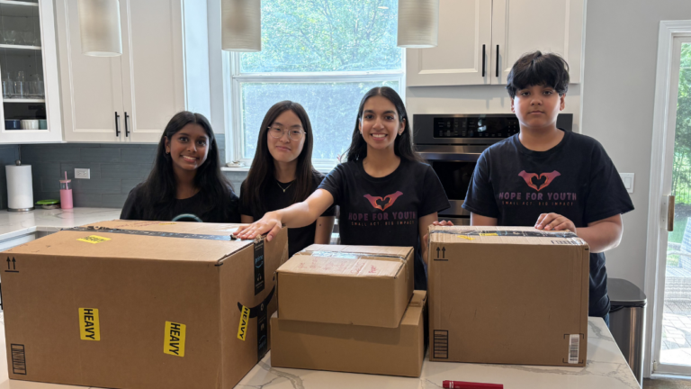 Aahana and Vihaan Chawla stand with two volunteers behind boxes of donations