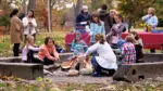 Group of kids and parents gathered around a bonfire roasting hot dogs after a hayride in Naperville