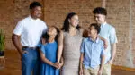A family look at each other with smiles on their faces in a room with brick walls.
