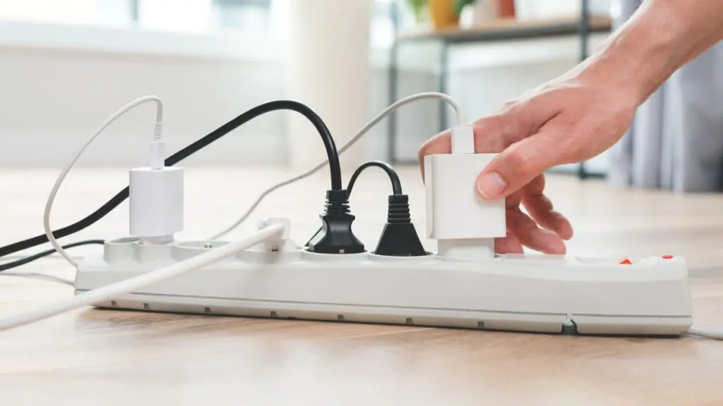 Close up of power cord with multiple things plugged in and hand plugging in another