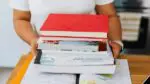 A person holds books in at a classroom desk