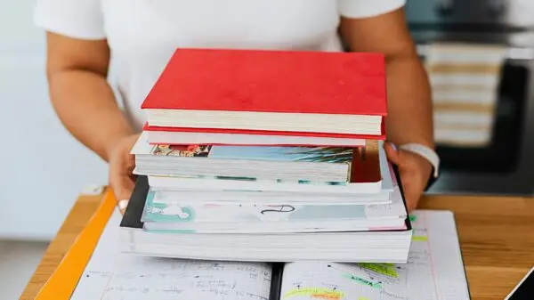 A person holds books in at a classroom desk