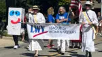 Members of the League of Women Voters of Naperville march in a parade dressed as suffragettes with another dressed is a ballot box.