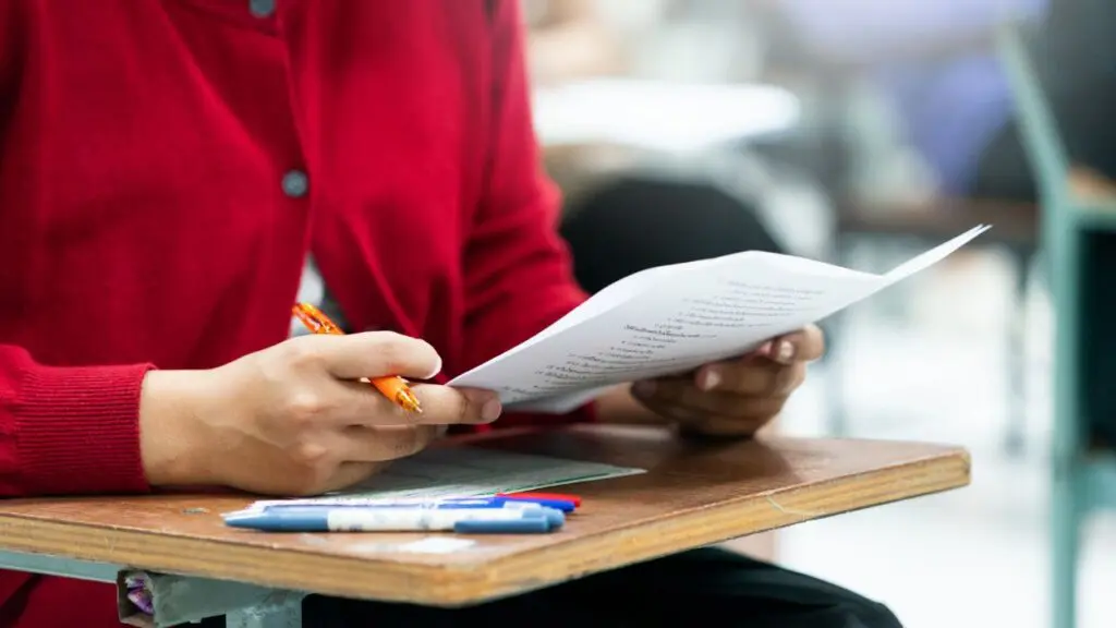 Close up of student holding paper and pen at desk