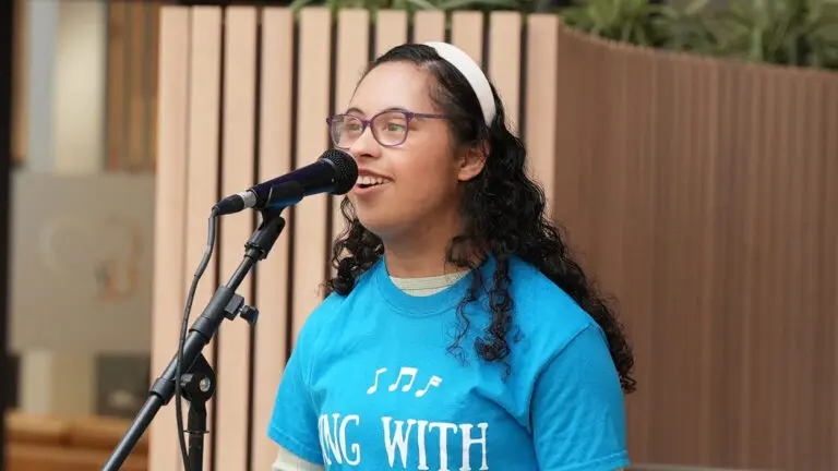 Eden Salem sings into a microphone in a blue t-shirt and white headband.