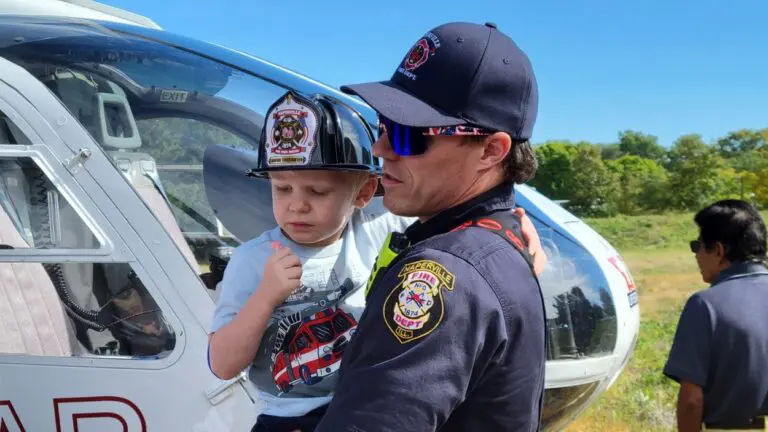 A member of the Naperville Fire Department holds a child wearing a plastic firefighter hat at the 2026 Public Safety Open House