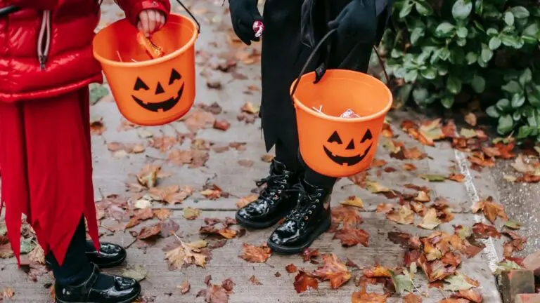 Two children holding plastic trick-or-treat buckets, leaves are on the ground