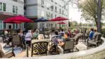 Residents of Martin Avenue Apartments sit at dining tables on the patio with red umbrellas.