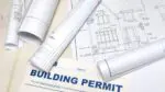 building design plans rolled up with a building permit slip nearby