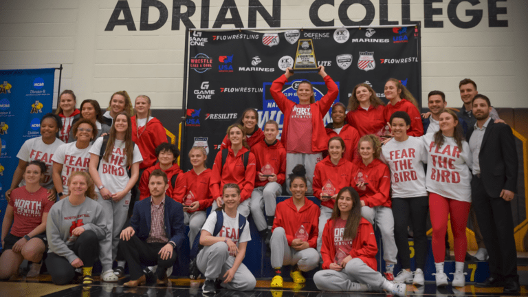 The North Central College women's wrestling team gathers for a team photo, with Yelena Makoyed in the center of the back row holding the team's trophy