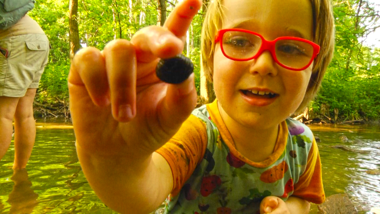 Kid holds up rock during Woodland Family Hike