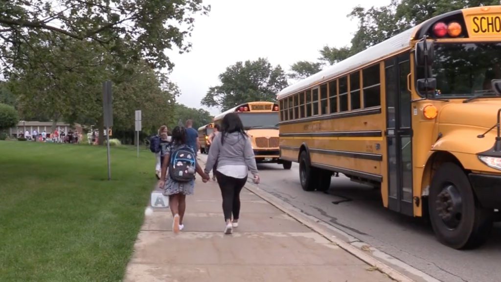 Parent and student walking on sidewalk next to school buses