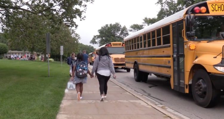 Parent and student walking on sidewalk next to school buses