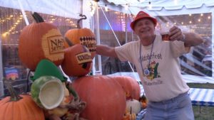 Man at Oktoberfest by carved pumpkins toasts camera