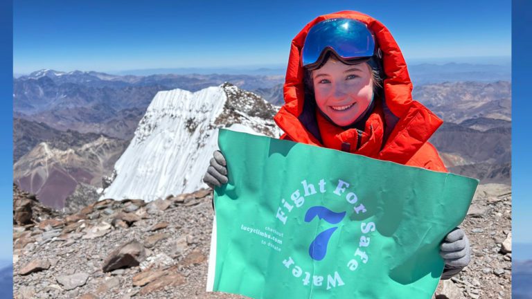 Lucy Westlake on a mountain holding fight for safe water sign