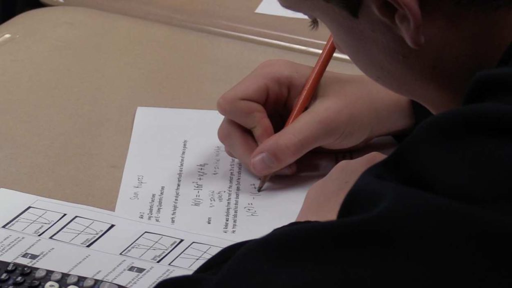 close up of student writing with pencil on paper