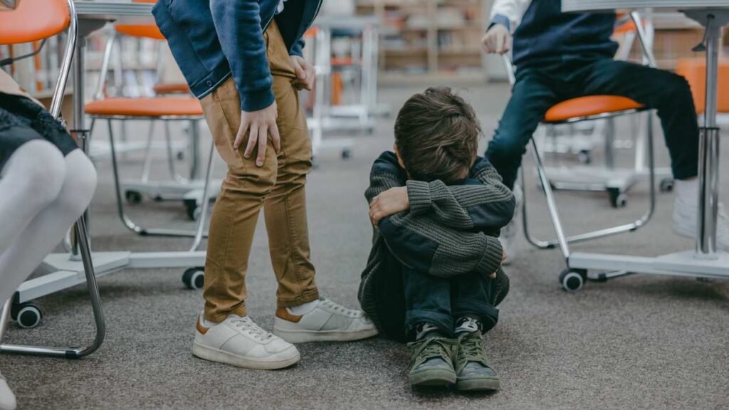 stock image of bullying, boy sitting with arms folded, head in arms on ground as others look on