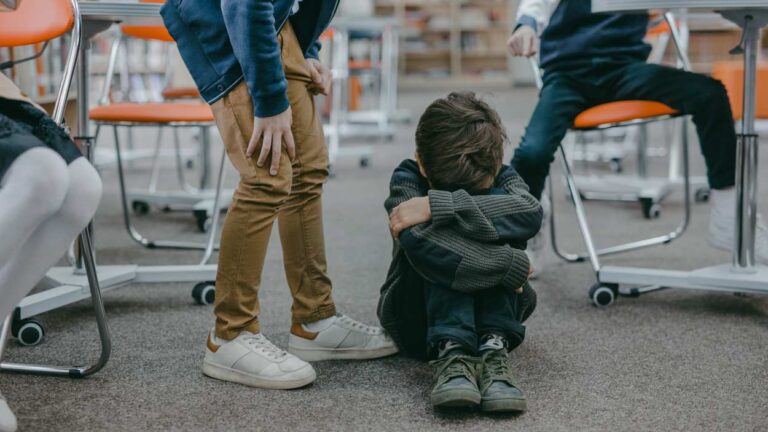 stock image of bullying, boy sitting with arms folded, head in arms on ground as others look on