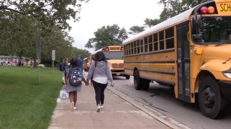 Child walking with adult by school buses as they head back to school