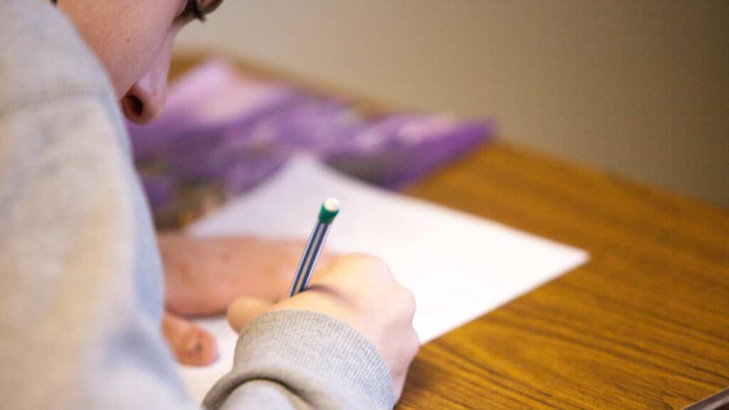 Close up student writing on paper on desk